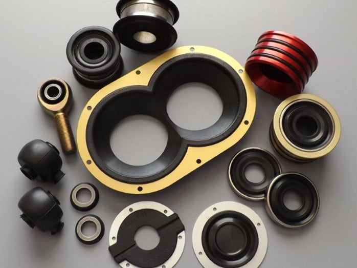 A collection of metal and rubber automotive parts on a gray background, including bearings and bushings in varied shapes and colors. Mechanical, industrial theme.