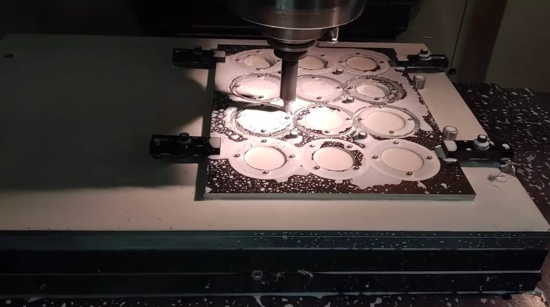 A CNC machine precisely cuts circular patterns into a metal sheet, surrounded by metal shavings, under bright lights in a workshop setting.